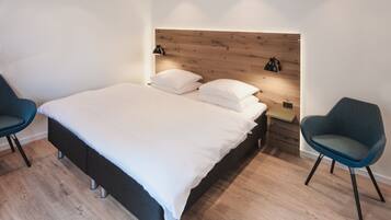 A modern bedroom with a wooden headboard, a large bed with white linens, two bedside tables with lamps, and two blue chairs.