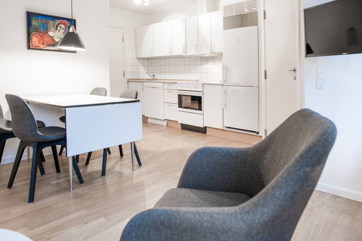 A modern kitchen with white cabinets, a dining table with chairs, and a gray armchair.