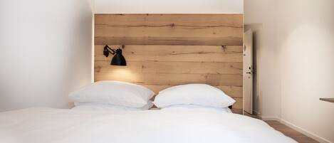 Une chambre à coucher avec une tête de lit en bois, deux oreillers blancs et une lampe noire fixée au mur.