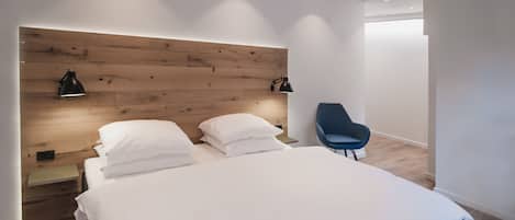 A modern bedroom with a wooden headboard, a single bed with white bedding, a blue chair, and two wall-mounted lamps.