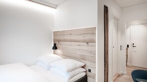 A modern bedroom with a wooden headboard, a bed with white bedding, a black bedside lamp, and a blue chair. - Hotel Town Living (Ringkobing)