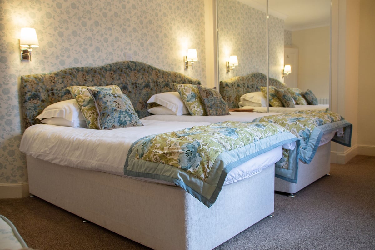 A double bed with floral headboard and matching pillows, a nightstand, and a mirror above the bed.