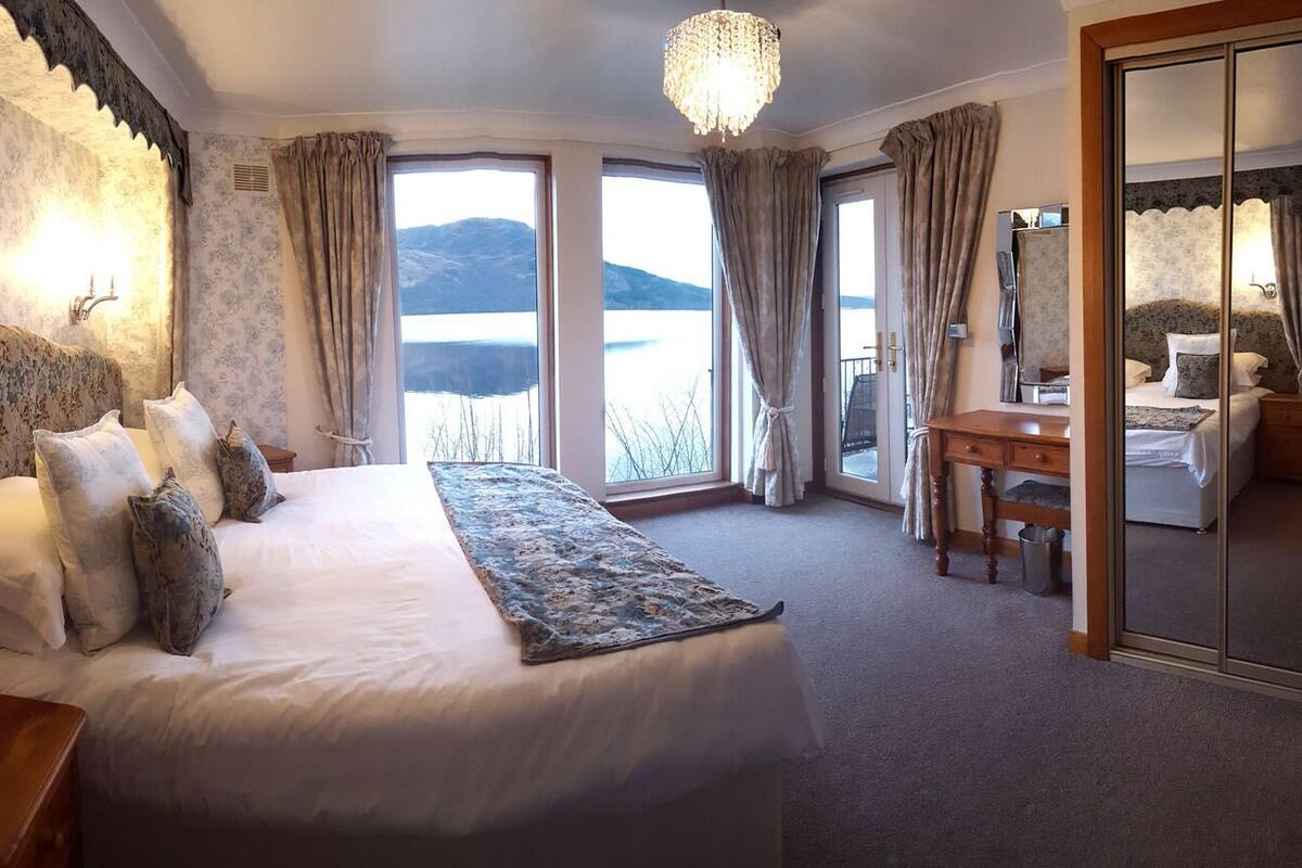 A hotel room with a large bed, a desk, and a view of the mountains through the windows.