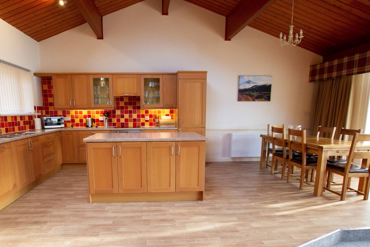 A spacious kitchen with wooden cabinets, a central island, and a dining area with wooden chairs and a table.