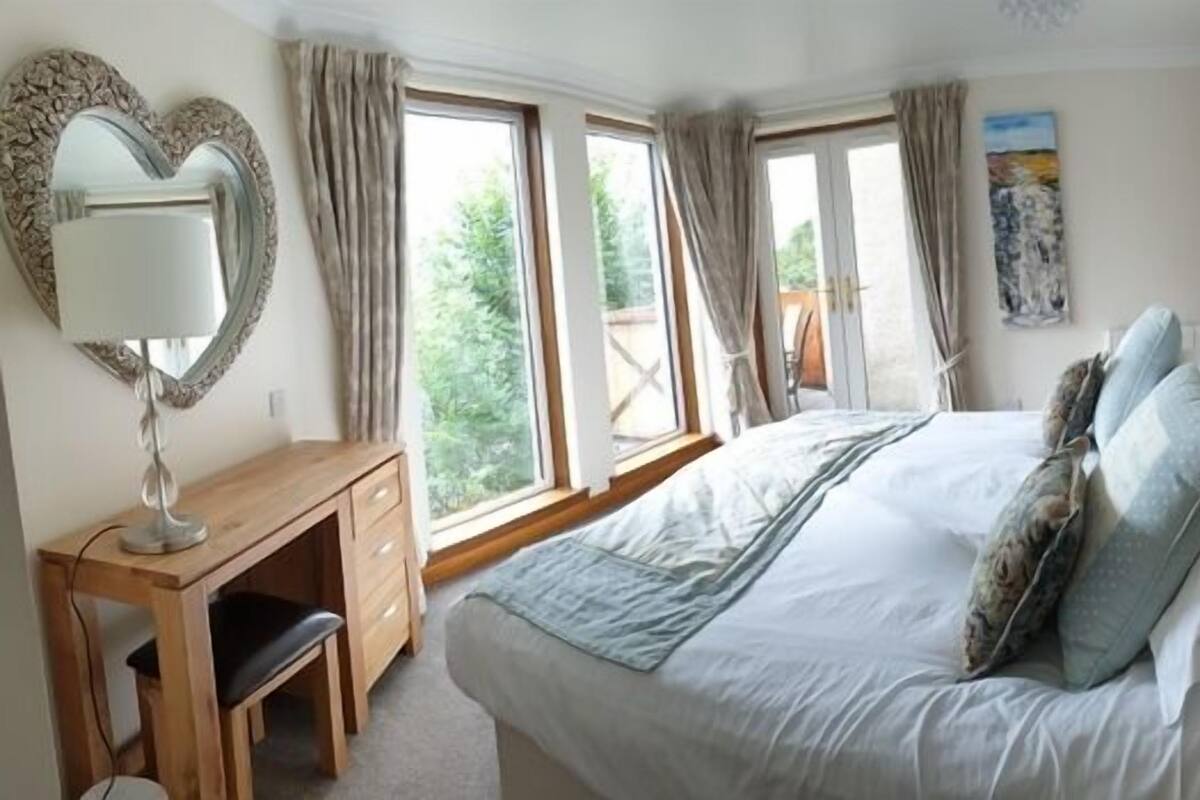 A bedroom with a bed, a desk, and a large window.