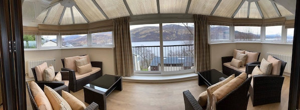 A cozy seating area with wicker furniture and a large window overlooking a lake and mountains.