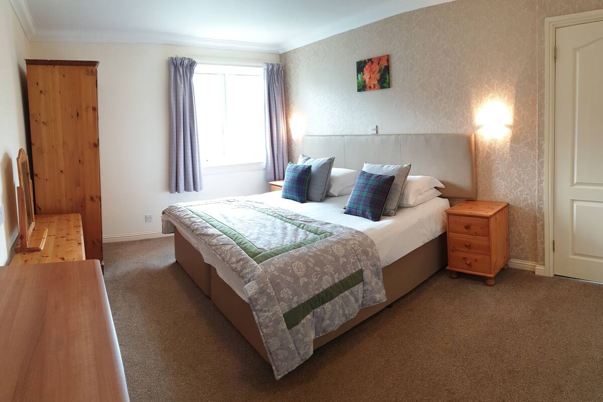 A bedroom with a bed, nightstand, wooden wardrobe, and a window with curtains.