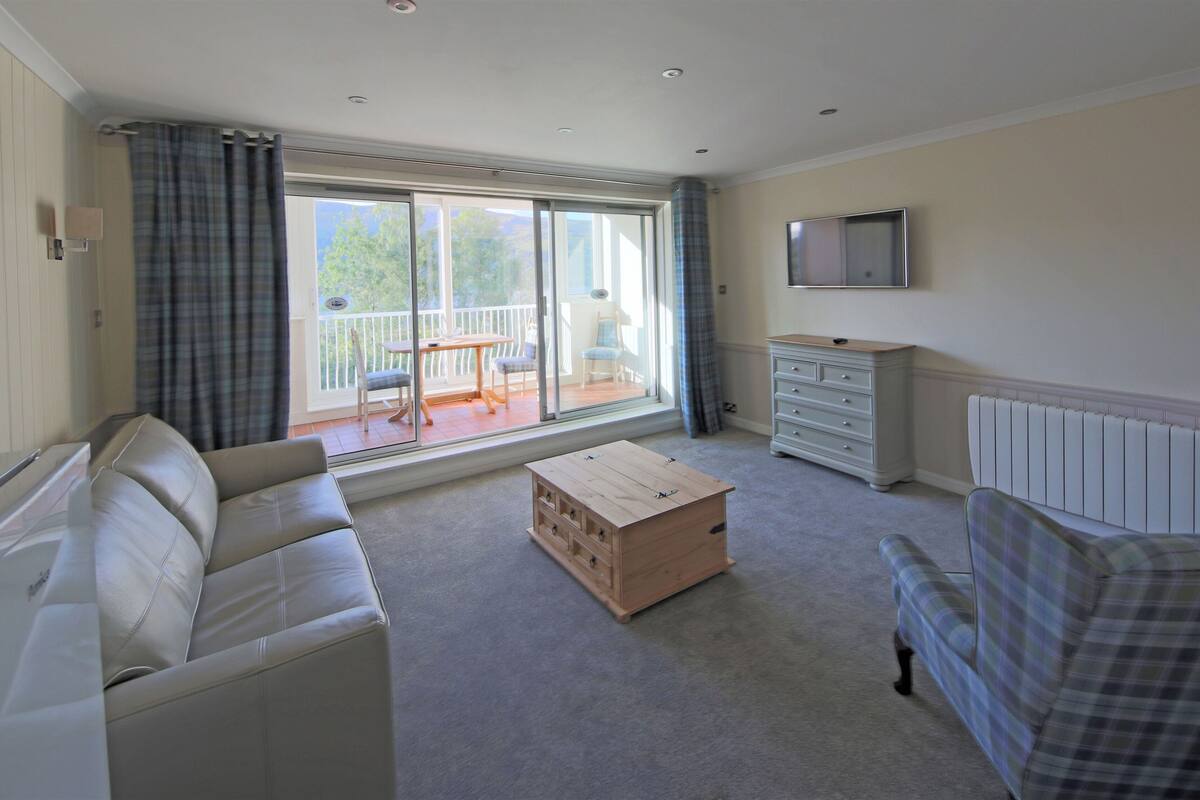 A living room with a sofa, a plaid sofa, a wooden chest of drawers, and a television on the wall.
