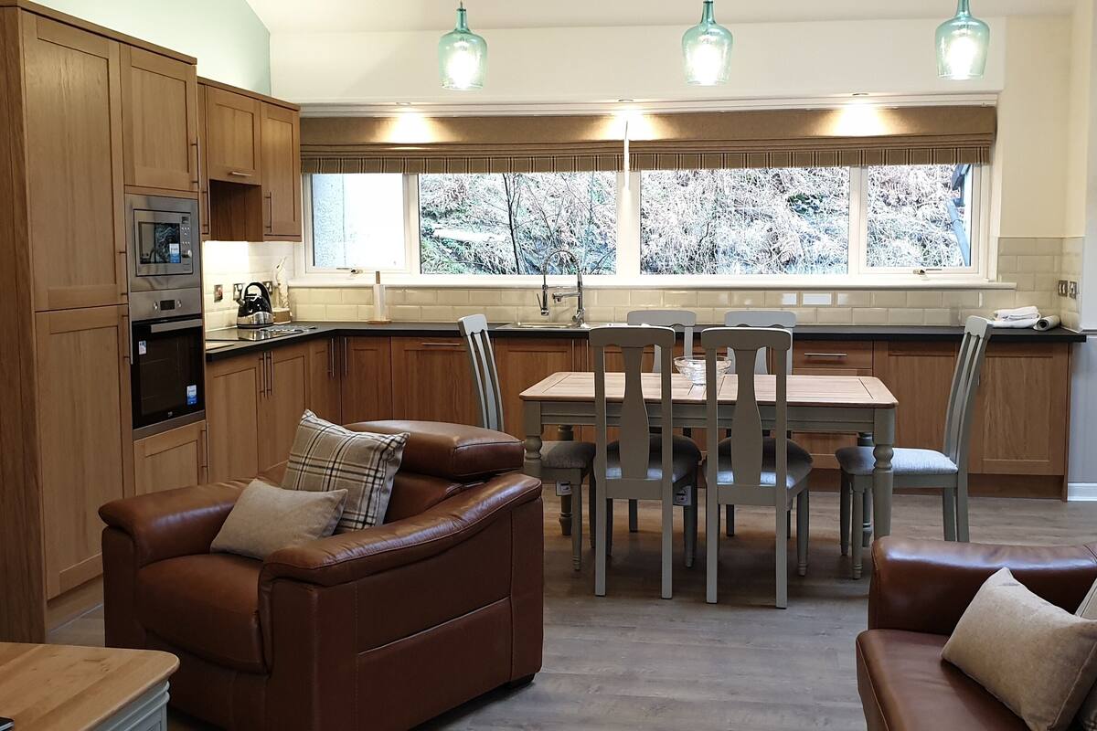 A modern kitchen with wooden cabinets, a dining area with a table and chairs, and a cozy seating area with a brown leather sofa.