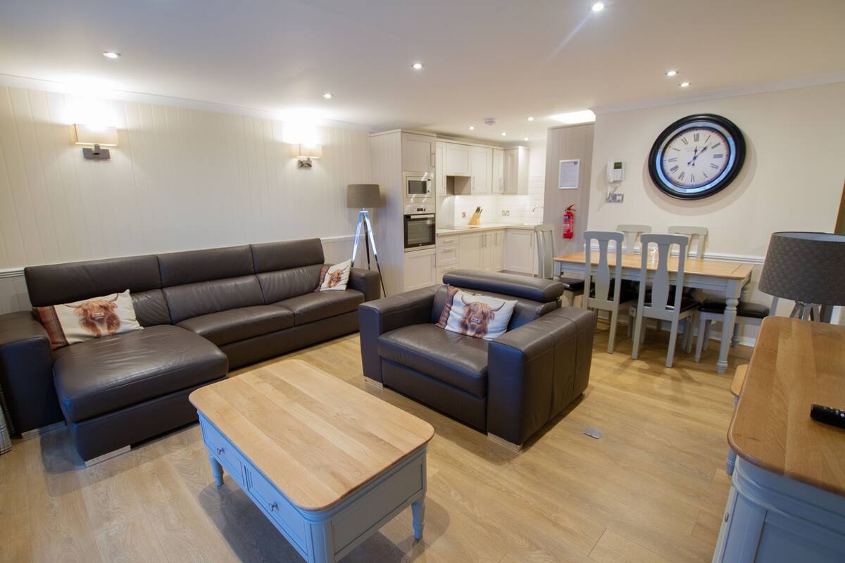 A modern living room with a sofa, two armchairs, a coffee table, and a dining area with a table and chairs.