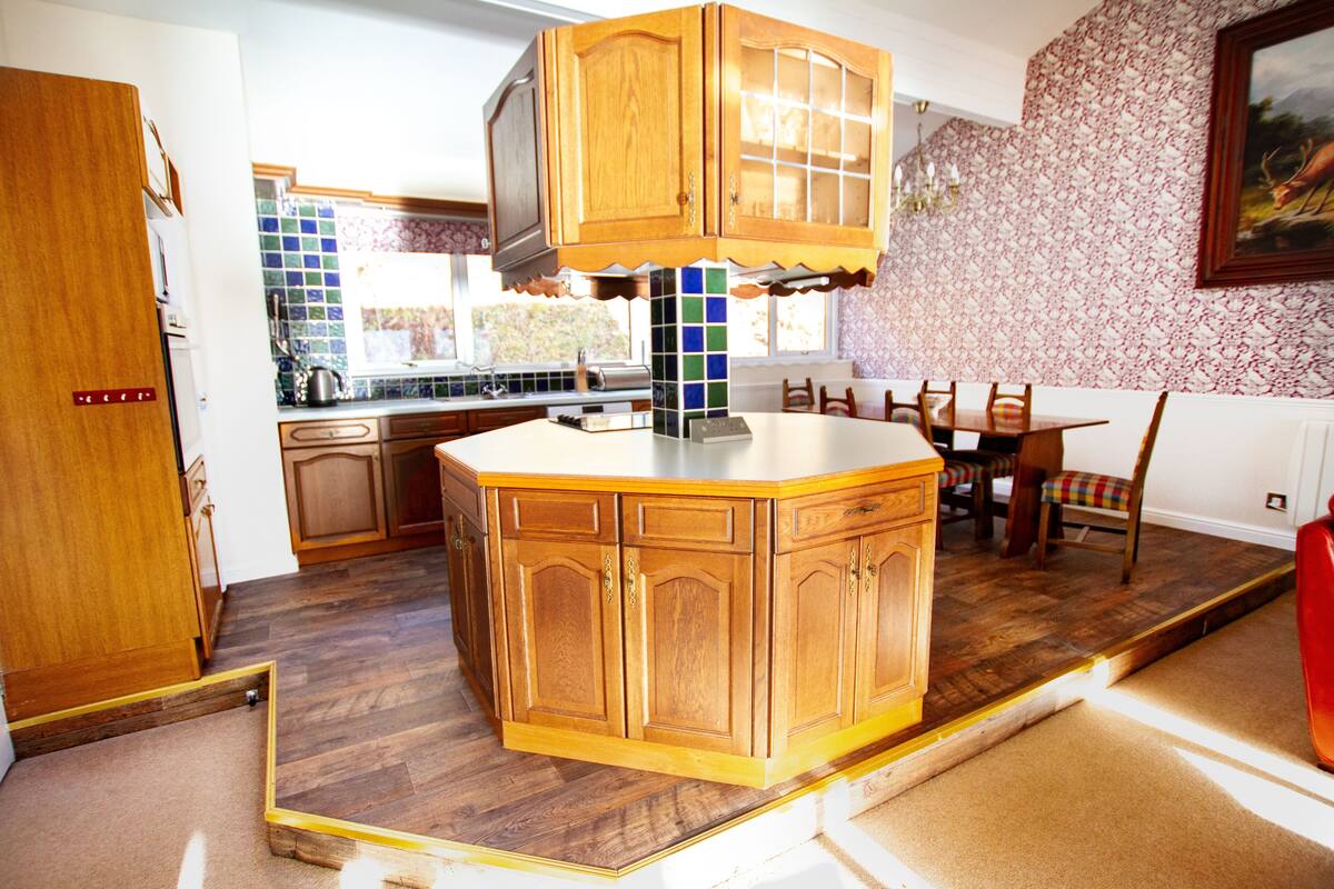 A kitchen with wooden cabinets, a tiled backsplash, and a dining area with chairs and a table.