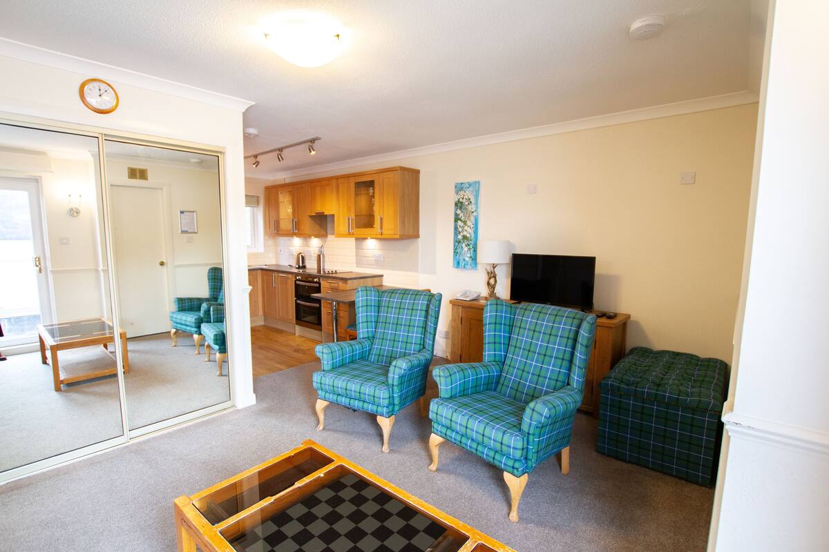 A living room with plaid armchairs, a coffee table, and a television.