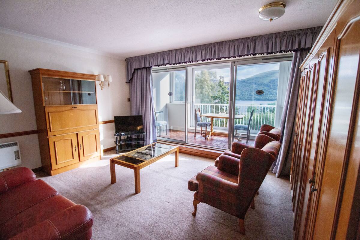 A living room with a sofa, armchair, and a glass coffee table. There is a wooden cabinet and a television.