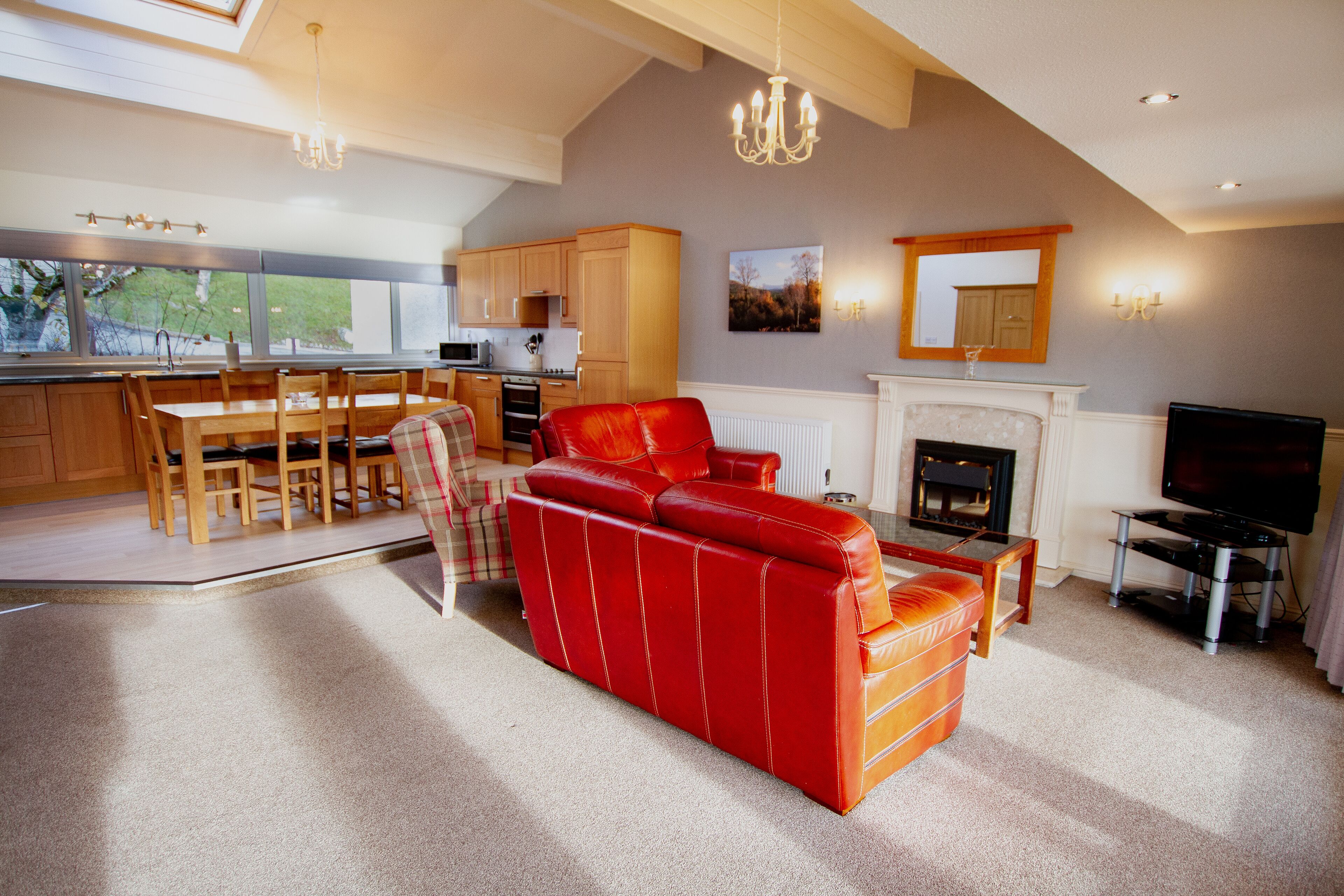 A spacious living area with a red leather sofa, a fireplace, a television, and a dining area with wooden furniture.