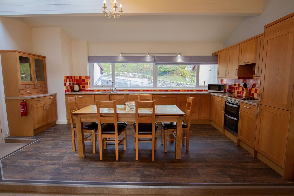 A kitchen with wooden cabinets, a dining table with chairs, a window with a view, and a microwave.