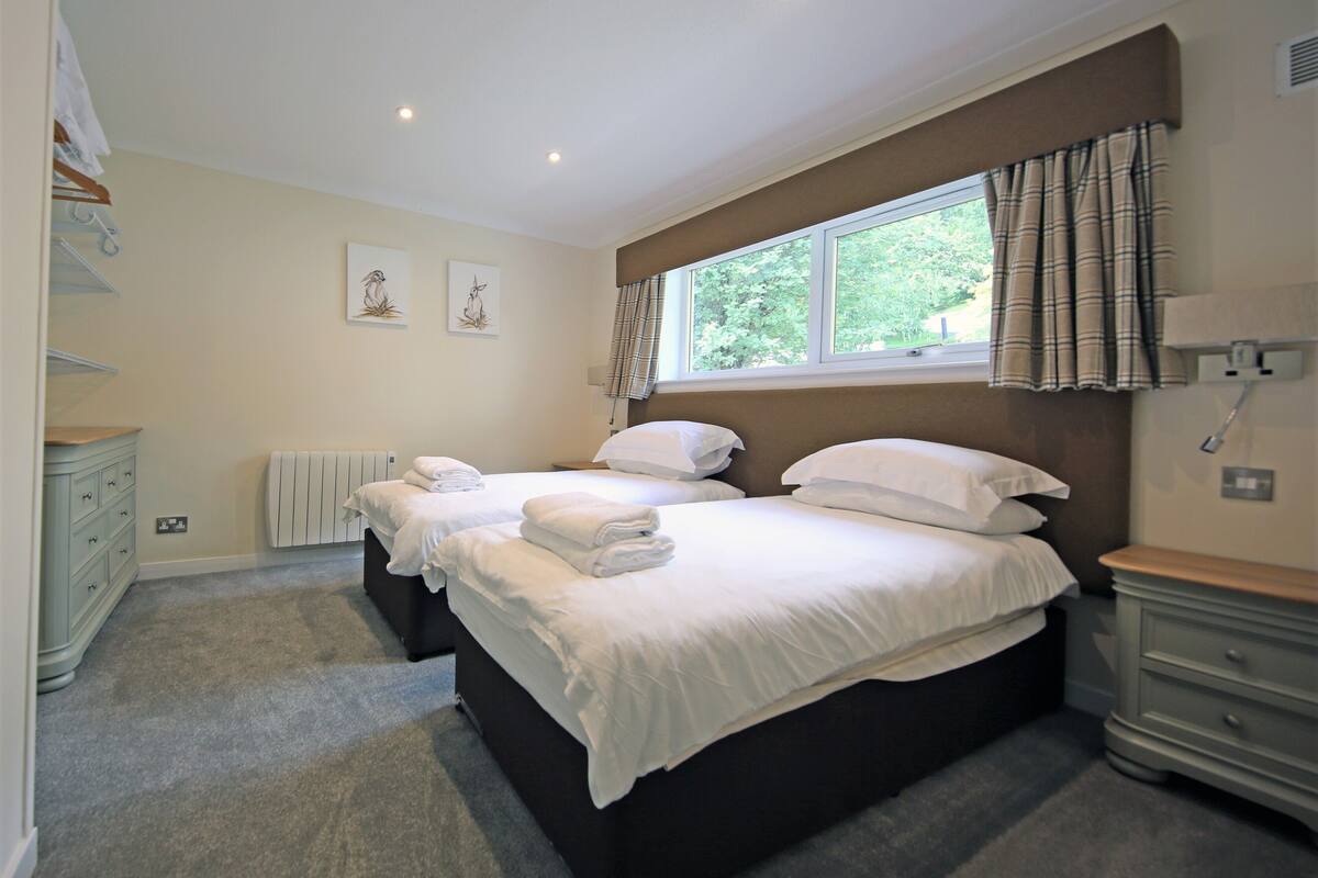 A bedroom with two beds, a window with curtains, a radiator, and a dresser.