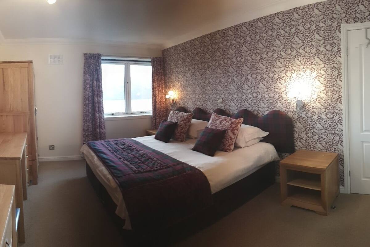A bedroom with a large bed, bedside tables, a wardrobe, and a window with curtains.