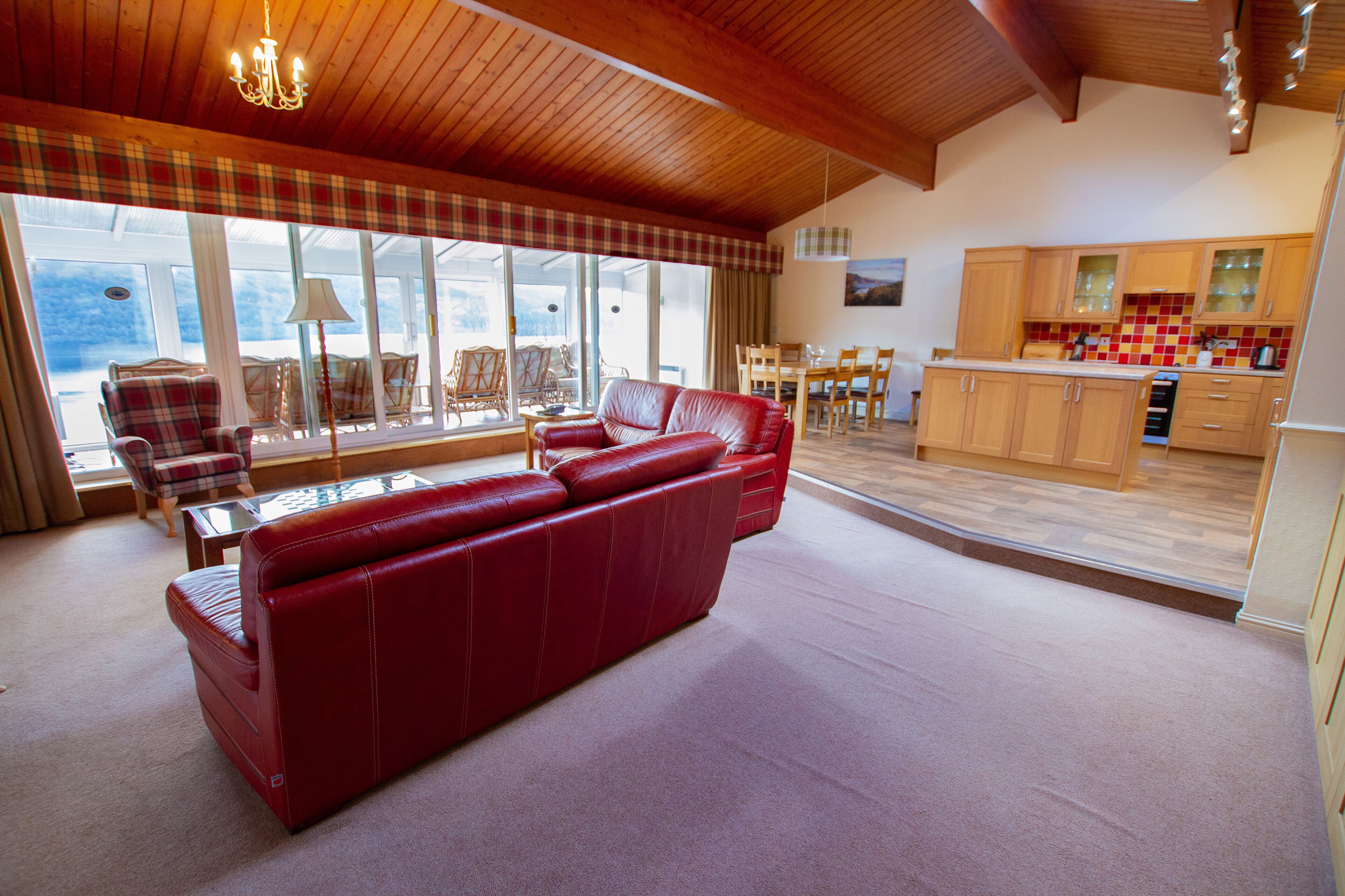 Ein geräumiges Wohnzimmer mit einem roten Ledersofa, einem Essbereich mit Holzsesseln und einer Küche mit Holzschränken.