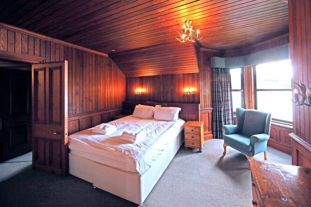 A wooden-paneled room with a bed, a chair, and a nightstand.