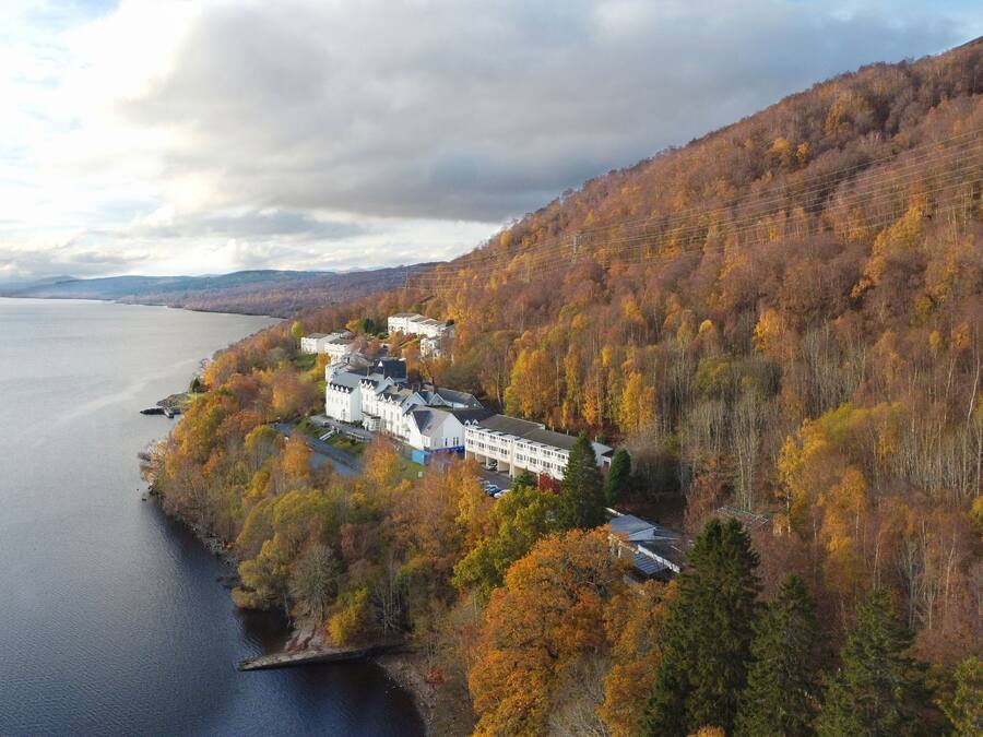 A lakeside property with a large building surrounded by autumn foliage.
