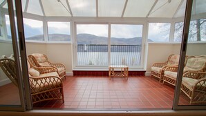 A sunroom with wicker furniture and a view of mountains. - Loch Rannoch Highland Club (Pitlochry)