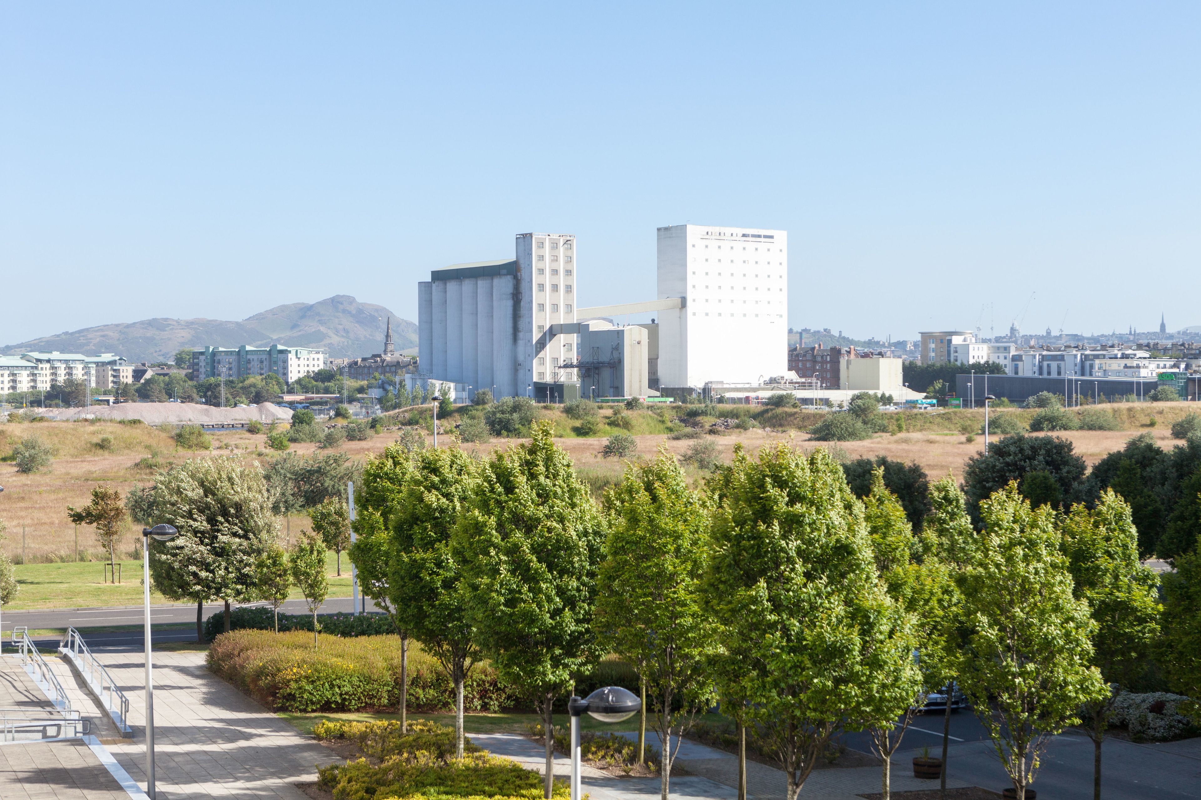 Un paysage urbain avec des bâtiments industriels et un espace vert comprenant des arbres et un sentier.