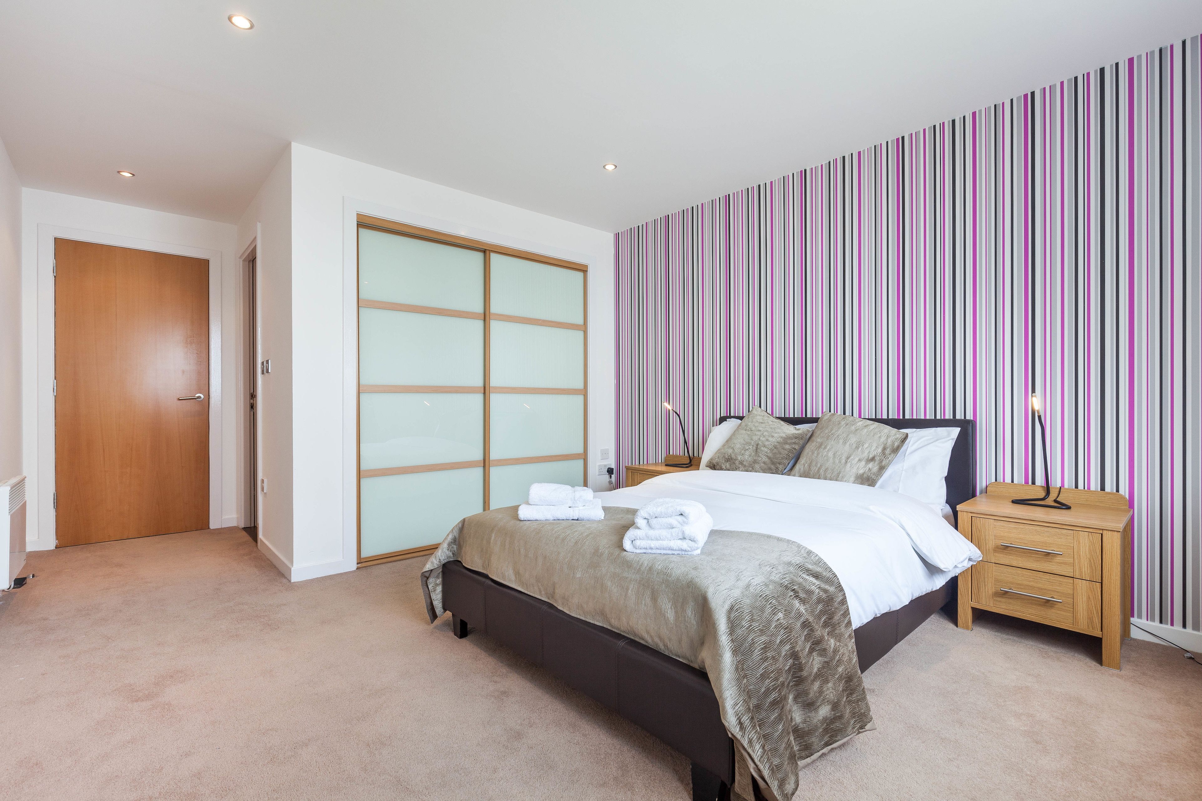 A bedroom with a bed, bedside tables, a wardrobe, and a striped wall.