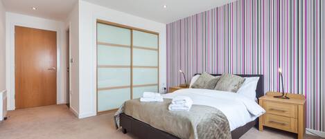 A bedroom with a bed, bedside tables, a wardrobe, and a striped wall.