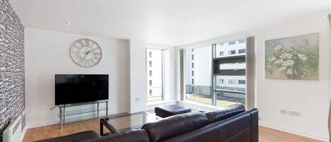 A modern living room with a large flat-screen TV, a brown leather sofa, a glass coffee table, and a stone wall.