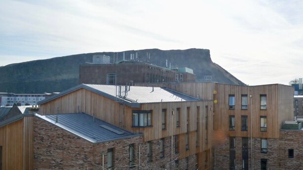 A modern building with a flat roof and large windows, set against a backdrop of a mountain and a clear sky. - Crags View Apartment (Edinburgh)
