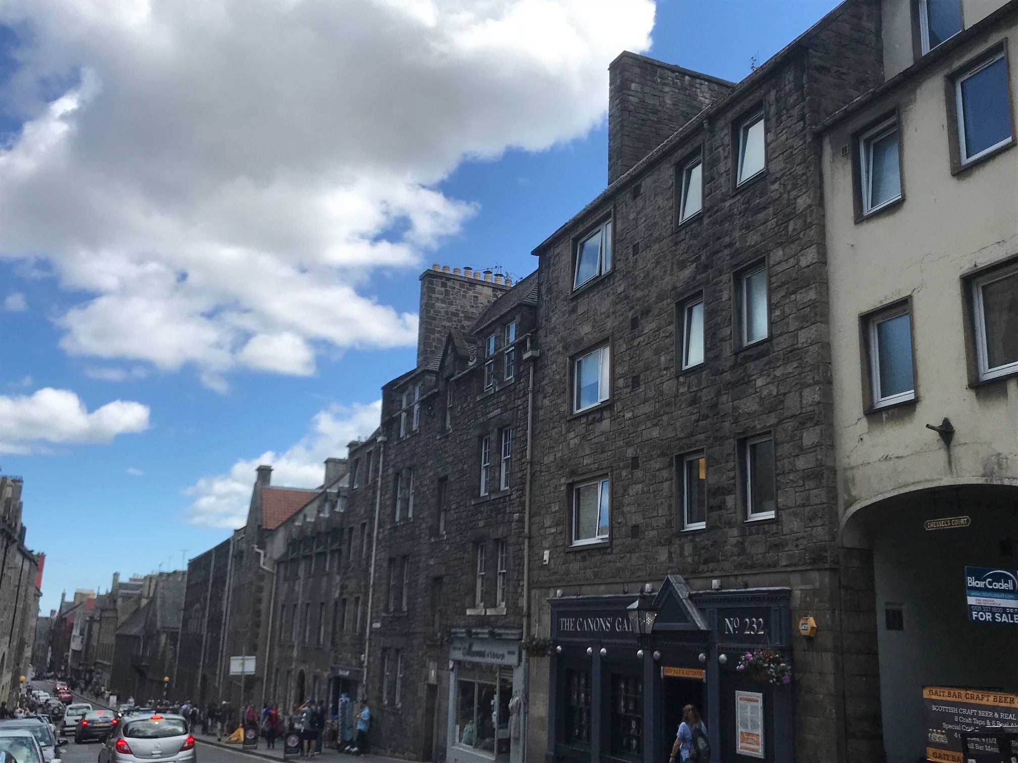 Eine Straße mit historischen Steinbauten, einem Pub namens "The Canons Gate" und einem Schild für "Blair Codell".