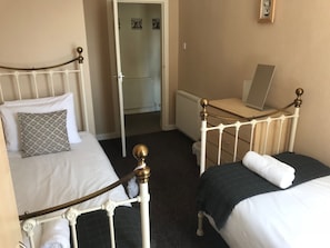 Ein Schlafzimmer mit zwei Einzelbetten, einem Schminktisch, einem Heizkörper und einem Laptop auf einem Schreibtisch.