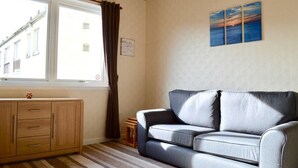 A room with a sofa, a cabinet, a window with curtains, and a painting on the wall. - Crags View Apartment (Edinburgh)