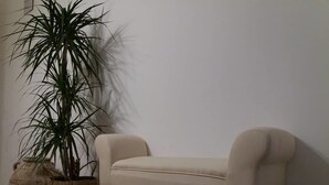 A beige sofa with wooden legs against a plain wall, accompanied by two large potted plants. - B&B Lei (Foggia)