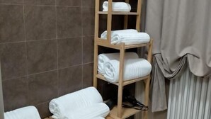 A bathroom with a wooden shelf holding towels and a toilet paper roll. - B&B Lei (Foggia)