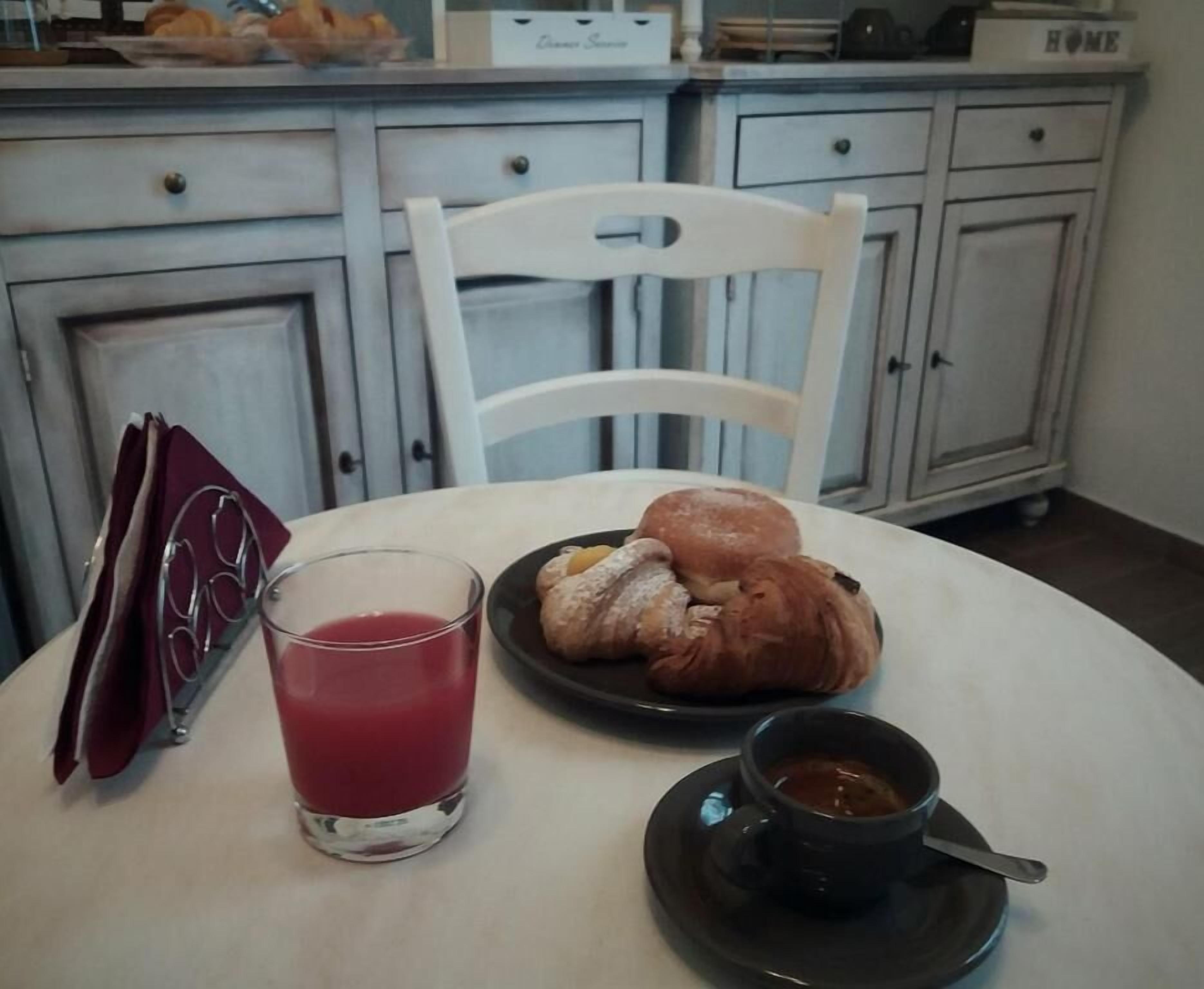 Uma mesa de jantar com um prato de doces, um copo de bebida vermelha e uma chávena de café.