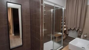 A modern bathroom with a glass-enclosed shower, a large mirror, and a white bathtub. - B&B Lei (Foggia)