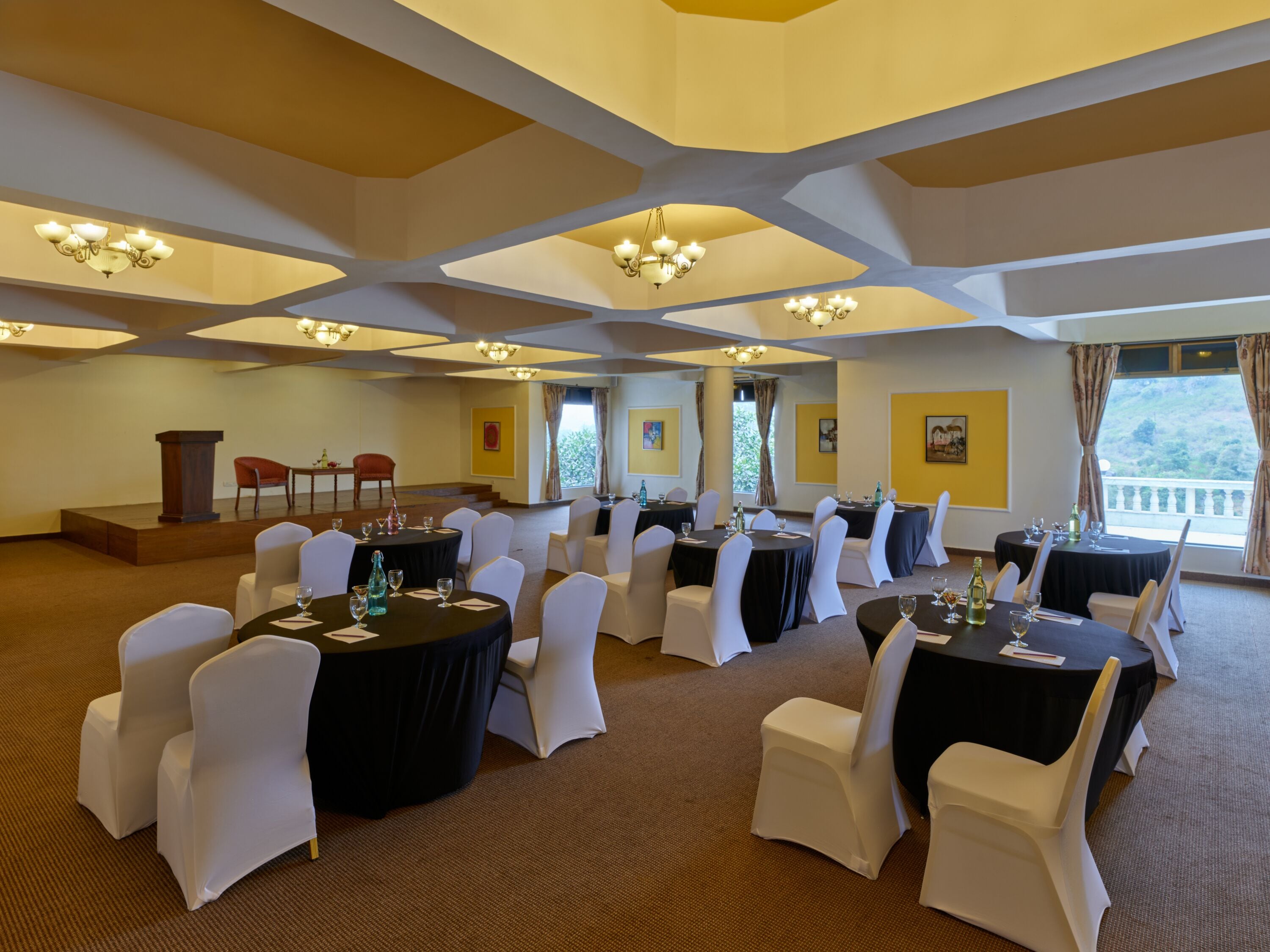 A conference room with round tables, white chairs, and chandeliers.