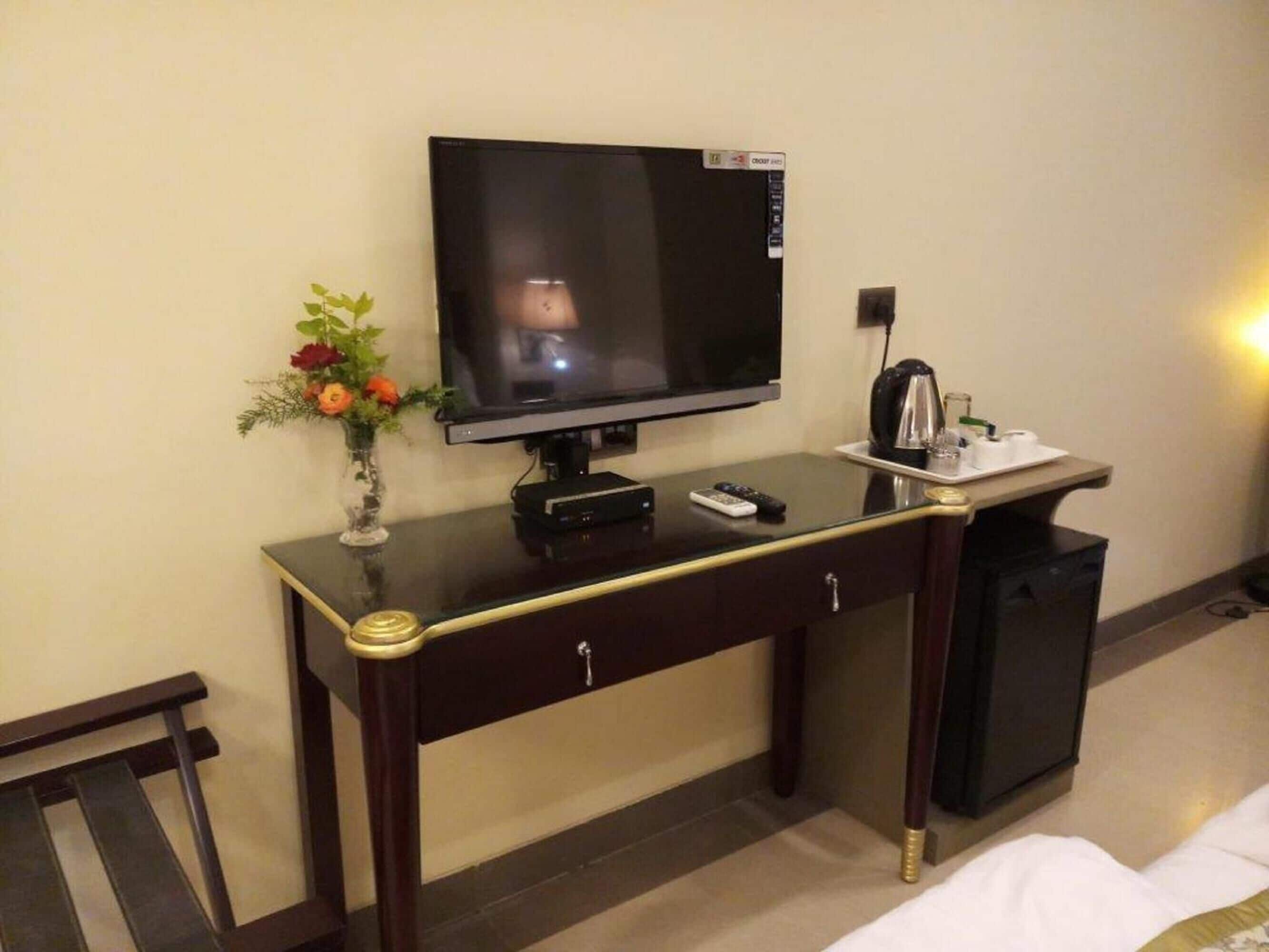 Hotelkamer met een televisie op een bureau, een vaas met bloemen, een waterkoker en een bed.