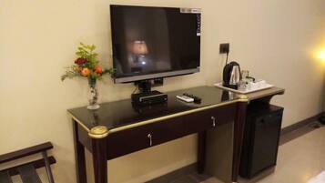 Hotelkamer met een televisie op een bureau, een vaas met bloemen, een waterkoker en een bed.