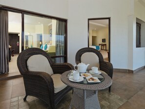 A room with wicker chairs and a glass table set with a teapot, cups, and cookies. - Sterling Mount Abu (Abu Road)