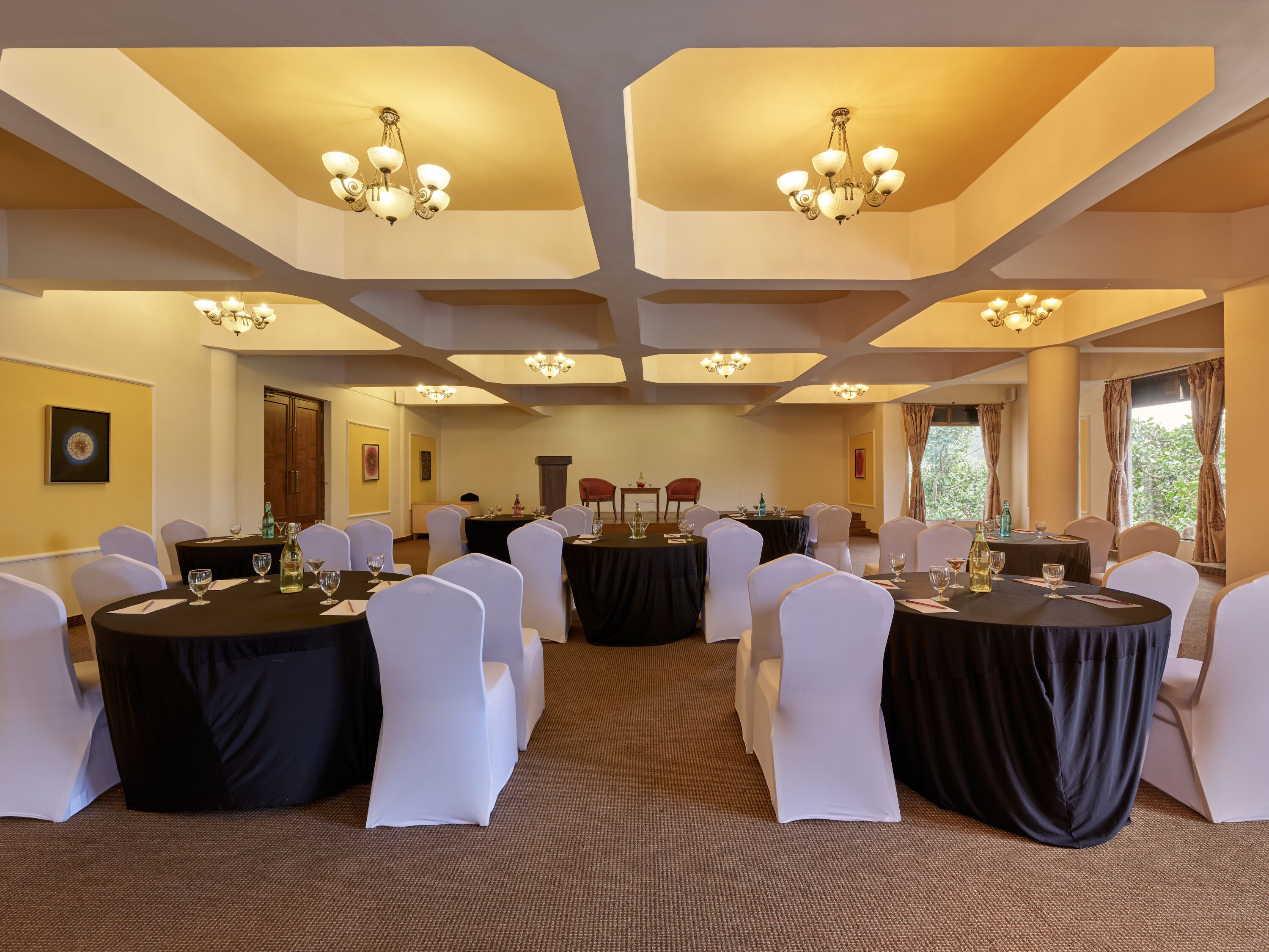 A conference room with round tables, white chairs, and chandeliers.