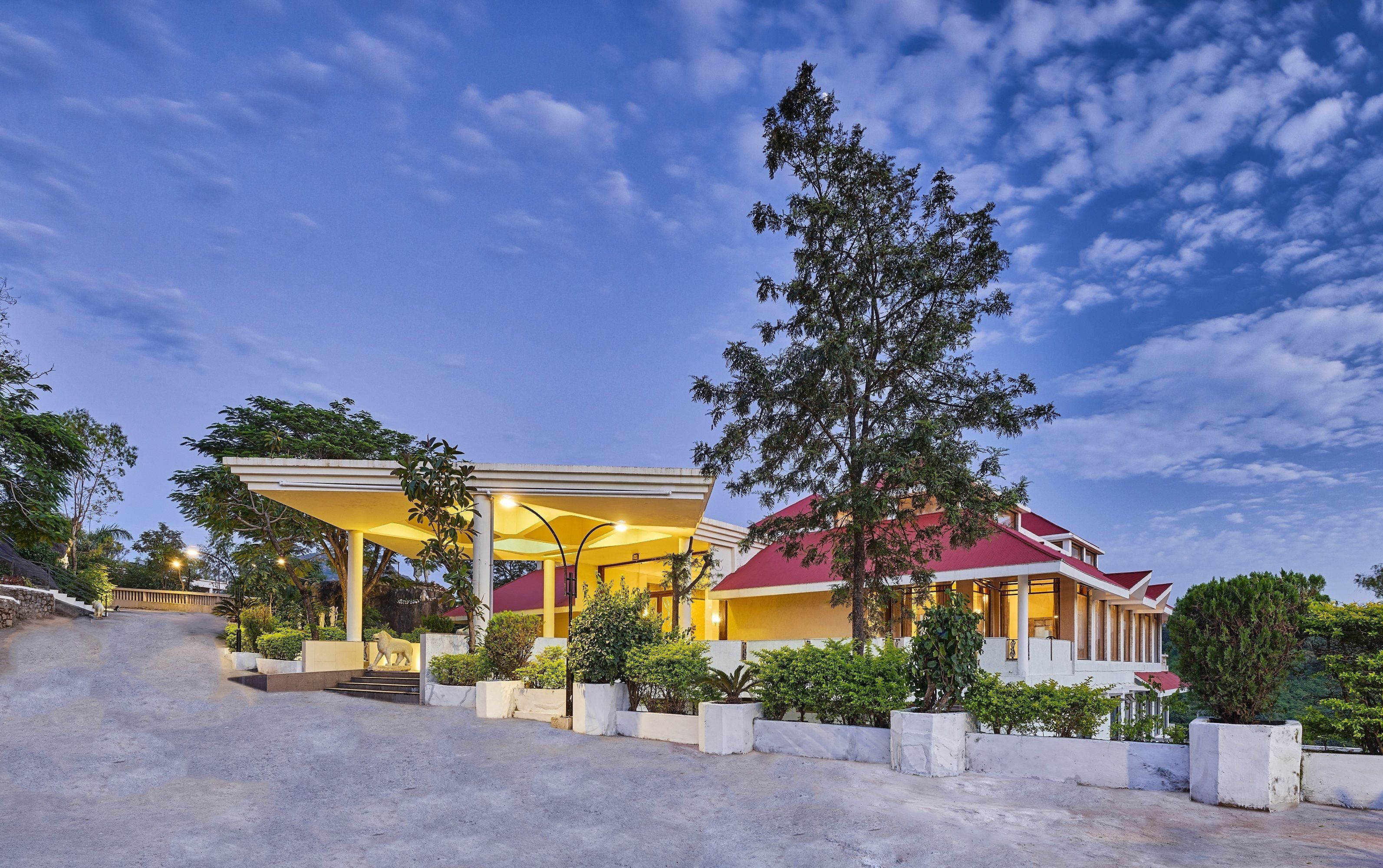A hotel with a covered outdoor area, steps leading to the entrance, and a red-roofed building.