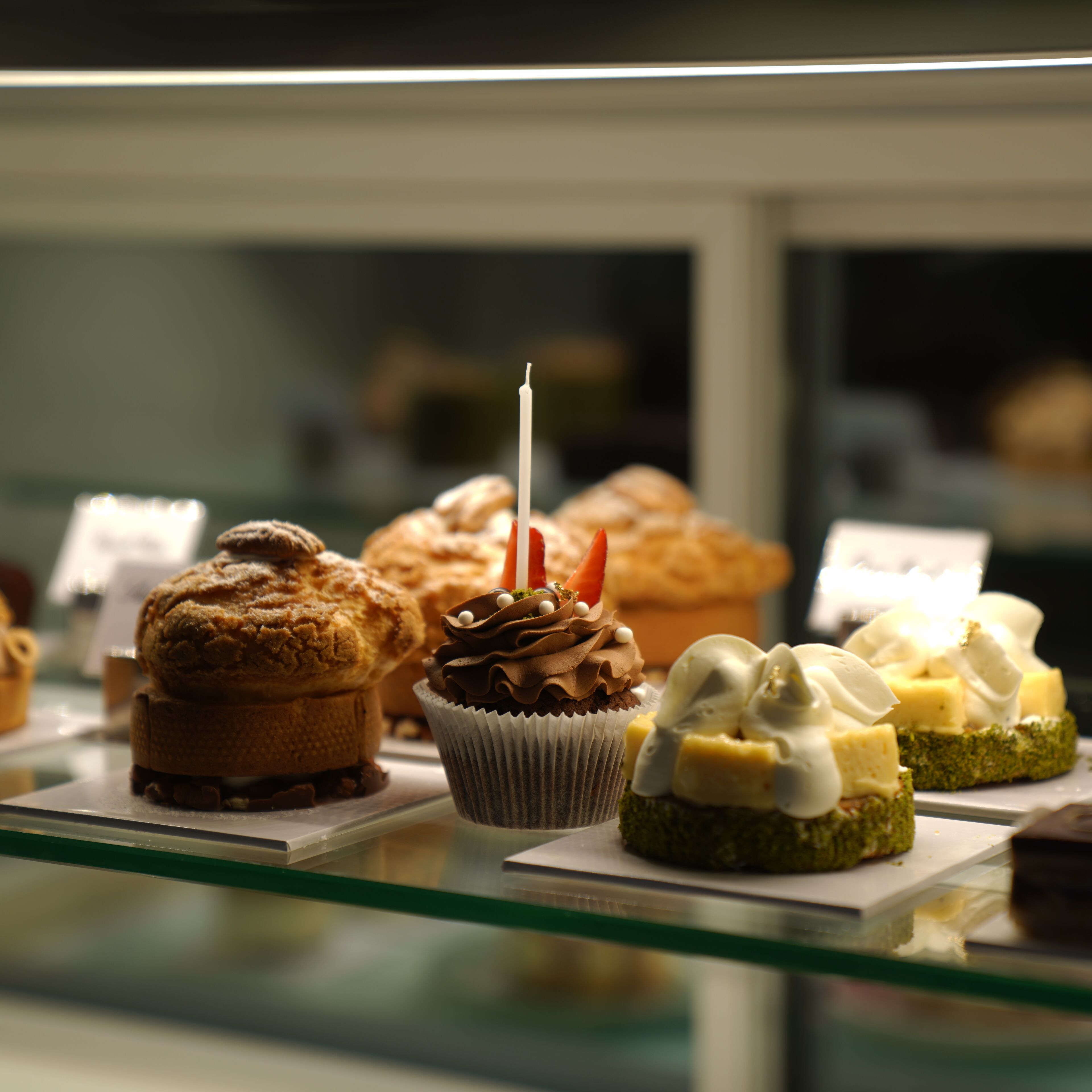 Une vitrine contenant divers produits de boulangerie, notamment des muffins et des cupcakes, dont l’un est décoré d’une bougie.