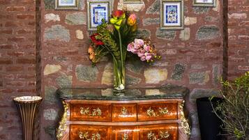 A room with a stone wall, a wooden dresser with gold handles, and a vase of flowers.