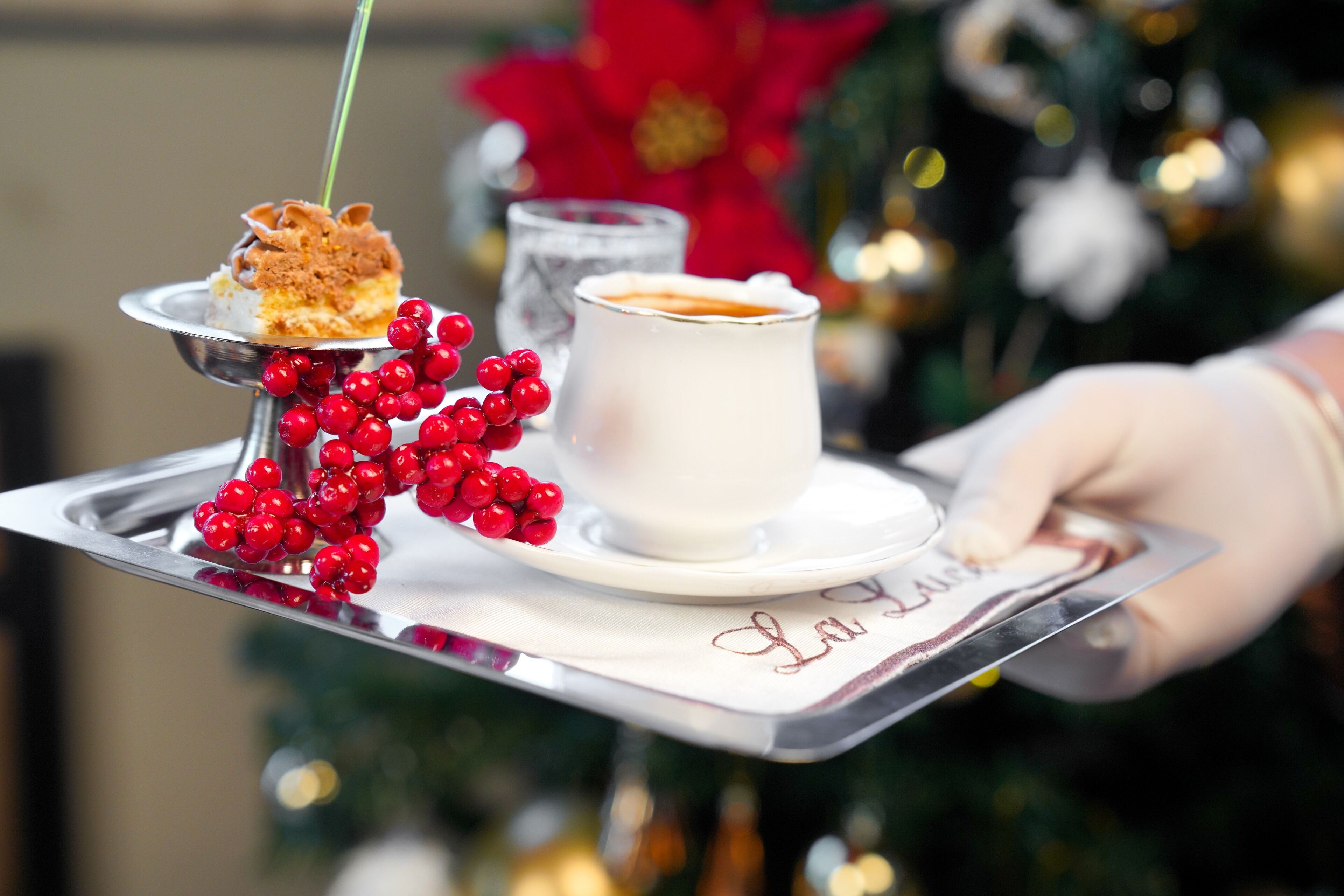A tray with a dessert and a cup of coffee, garnished with red berries, and a Christmas tree in the background.
