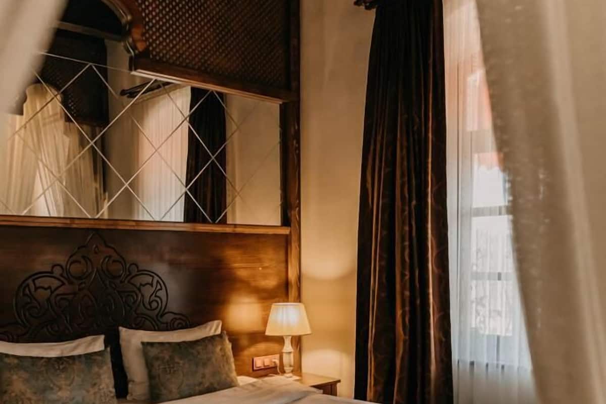 A bedroom with a bed, a nightstand, a lamp, and curtains.