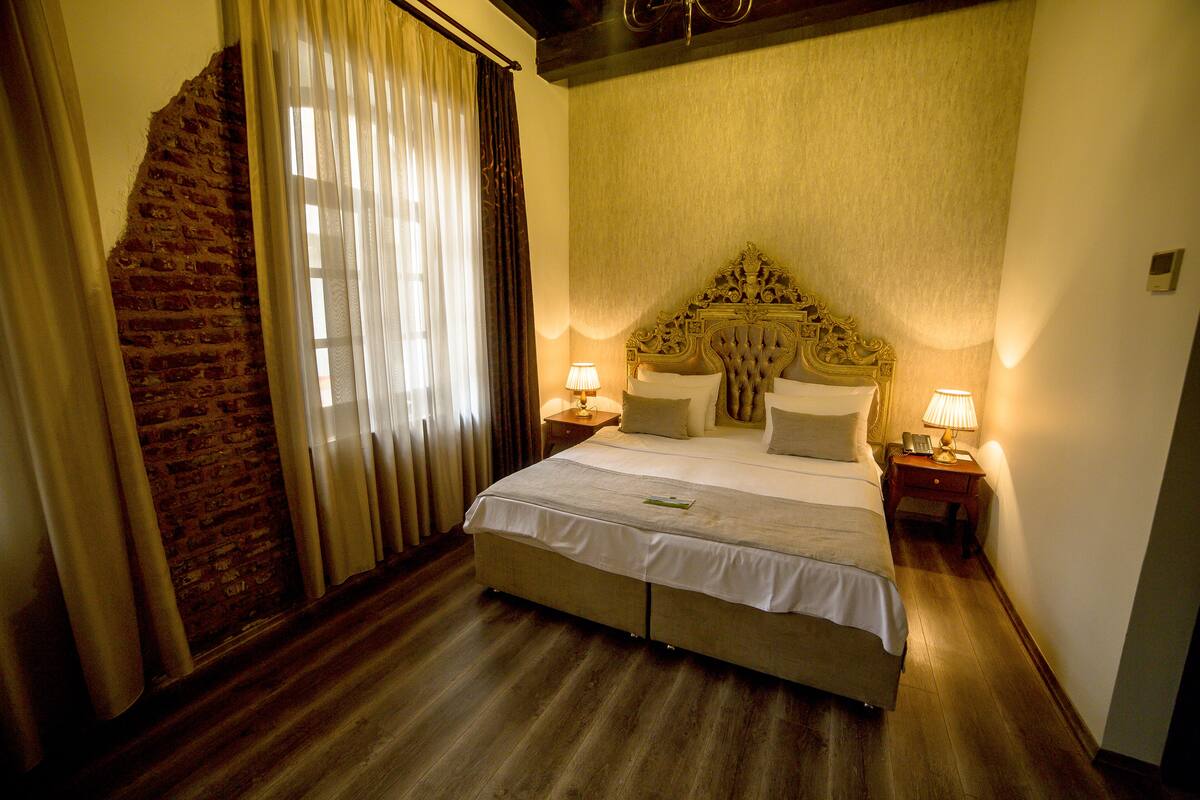 A hotel room with a large bed, wooden flooring, a brick wall, and two bedside lamps.