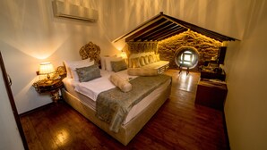 A bedroom with a large bed, a nightstand, a lamp, and a stone wall. - Panderma Port Hotel (Bandirma)