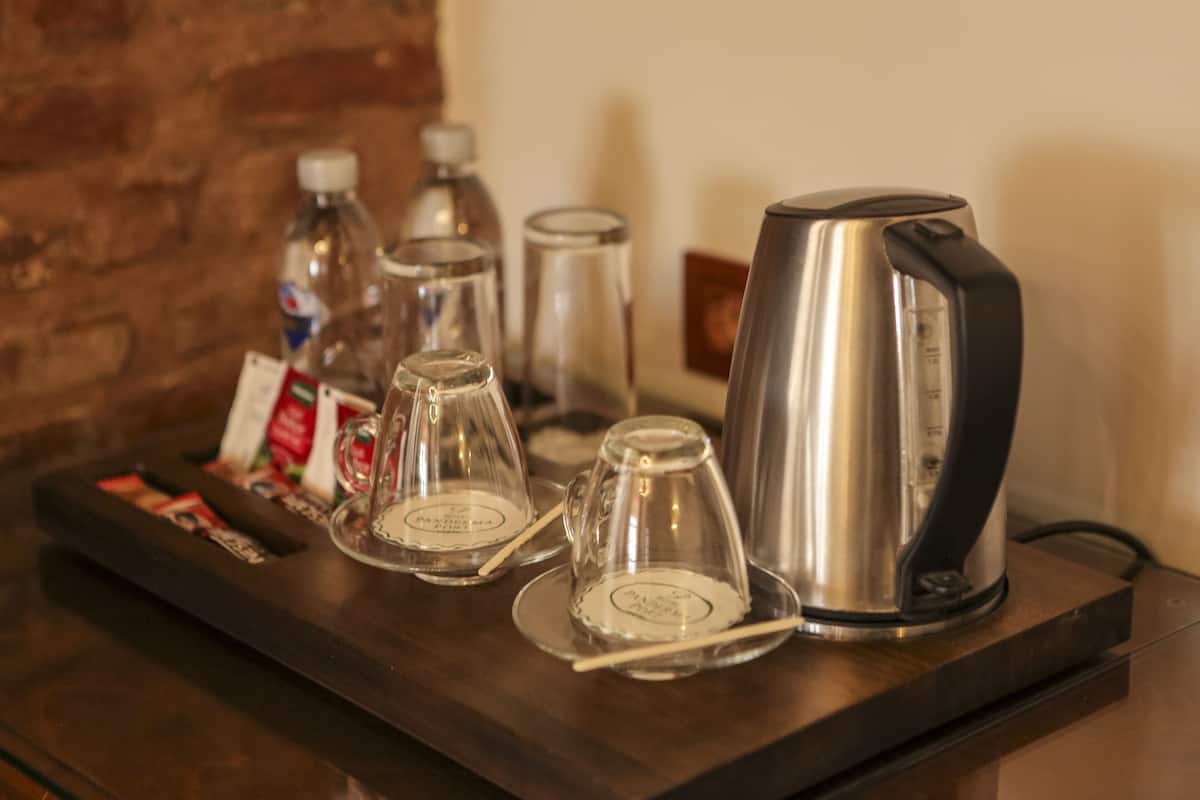 A coffee station with a kettle, glass cups, and condiments on a tray.
